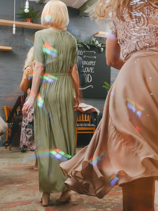 Female guests in long gowns at the loft-style venue — rainbow light beams on grey brick wall