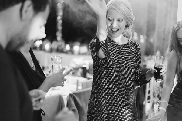 Smiling woman in black sparkly dress holds a glass, chats at the candlelit wedding dinner