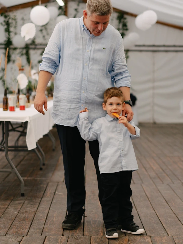 Man and young boy holding hands walking inside tent during wedding reception with balloon decorations.