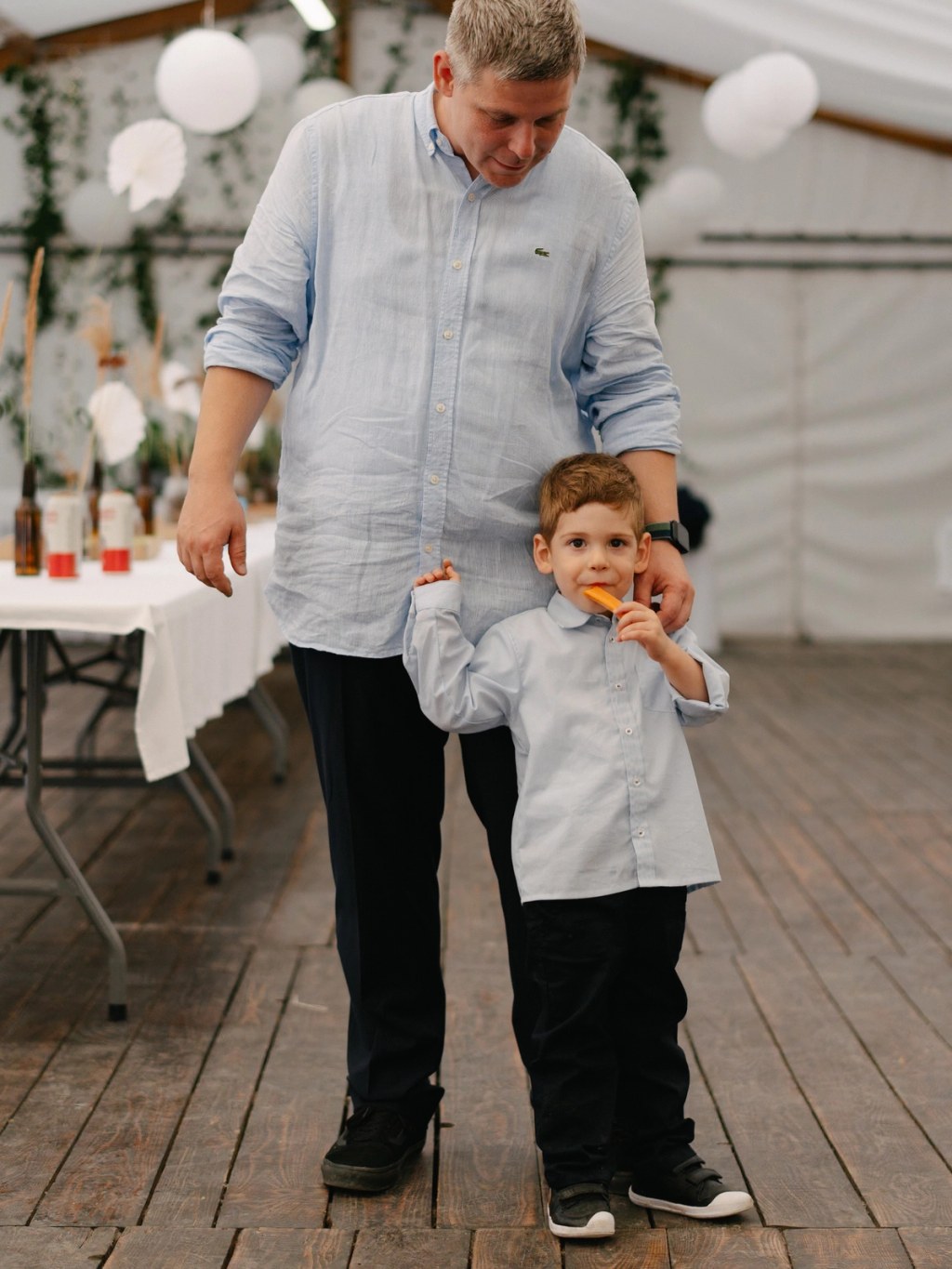 Man and young boy holding hands walking inside tent during wedding reception with balloon decorations.