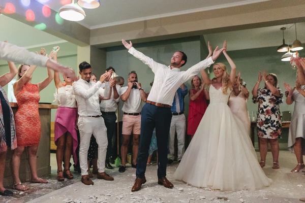 Bride and groom dance with arms raised celebrating at the reception — colourful lights illuminate the evening
