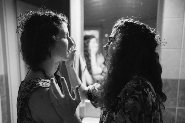 Black and white artistic portrait of two women getting ready in a bathroom, focusing on touch and connection.