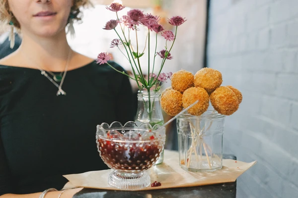 Woman in black beside a table with flowers, sweet balls and fruits in glasses, natural light