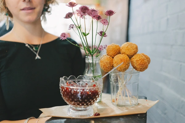 Woman in black beside a table with flowers, sweet balls and fruits in glasses, natural light