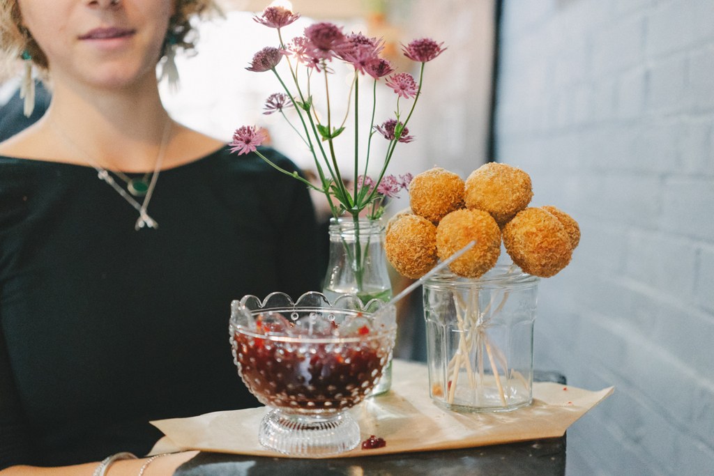 Woman in black beside a table with flowers, sweet balls and fruits in glasses, natural light
