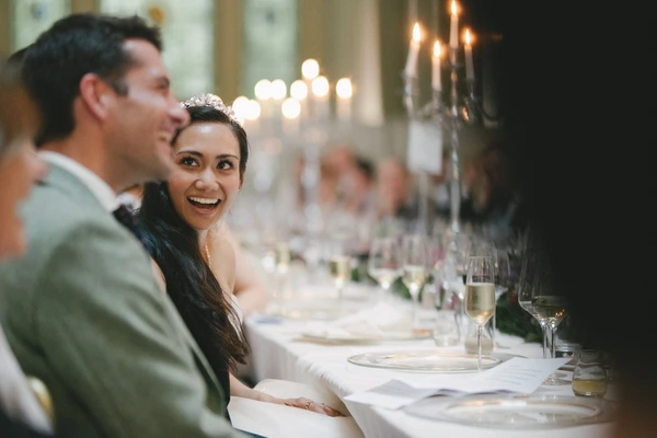 Bride wearing tiara glances back at her husband with a radiant smile at the wedding dinner