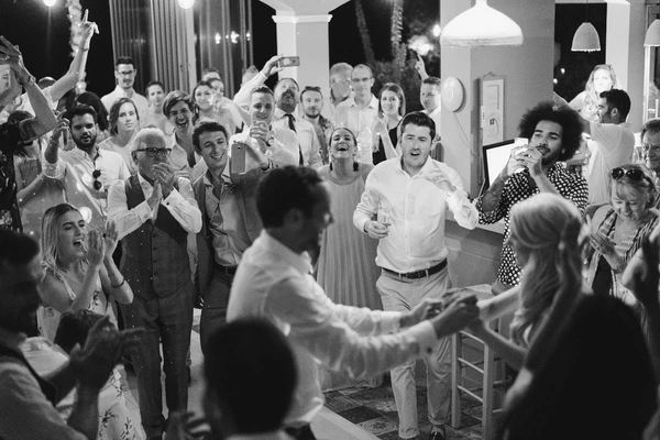 Wedding guests laughing and clapping by the dance floor at night — white shirts and elegant dresses