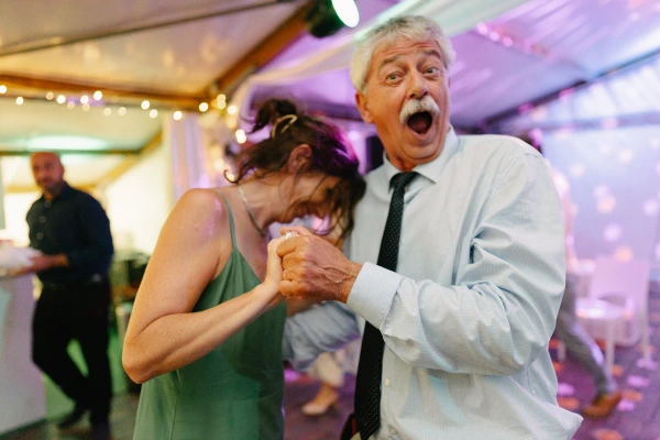 Elderly couple dancing at wedding party — colorful ambient lighting, joyful celebration, festive evening reception moment.
