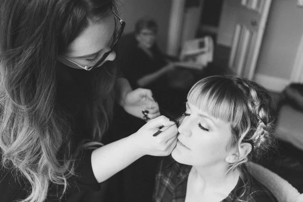 Makeup artist applies blush to the bride in a room — black-and-white close moment