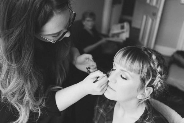 Makeup artist applies blush to the bride in a room — black-and-white close moment
