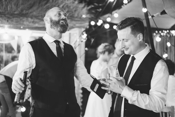 Two elegant men having a beer at the wedding party amid shiny decorations — celebratory mood