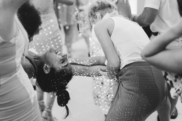 Bride in sparkling lace smiles beside the groom on the dance floor — black-and-white wedding party