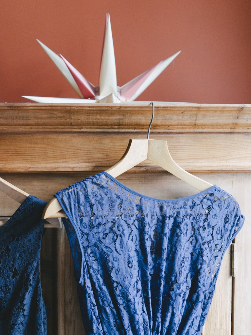 Blue lace dress on a white hanger in the dressing room beside a terracotta wall