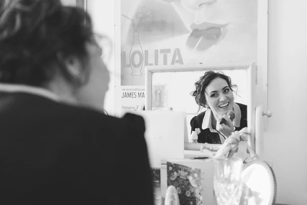 Bride smiles into the mirror on her wedding day — a joyful moment while getting dressed