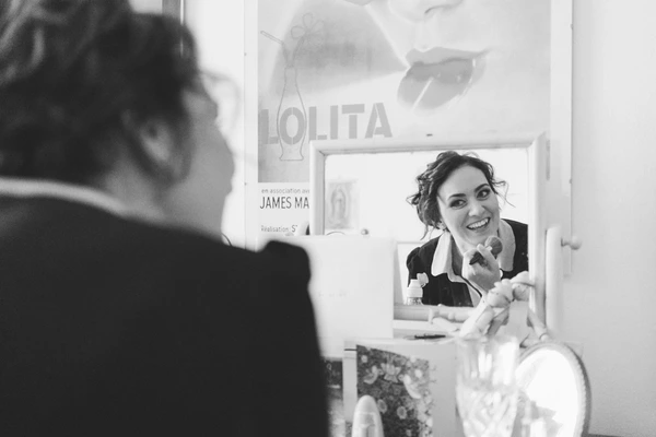 Bride smiles into the mirror on her wedding day — a joyful moment while getting dressed
