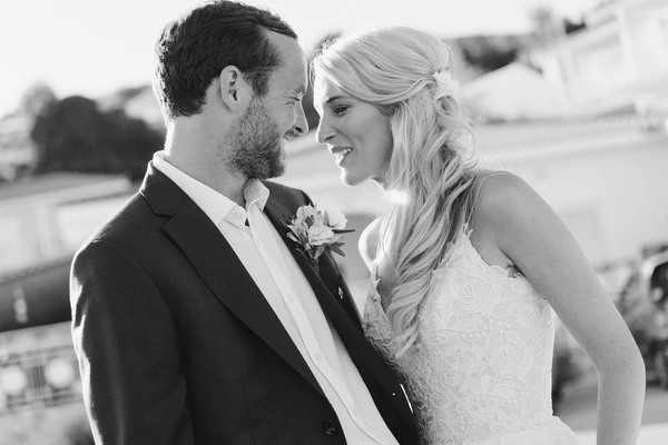 Bride and groom look lovingly at each other on an open terrace — fine lace dress. Black-and-white.