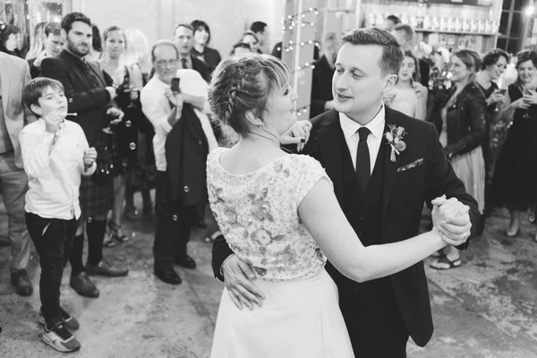 Bride and groom dance their first dance surrounded by guests — black-and-white, warm atmosphere