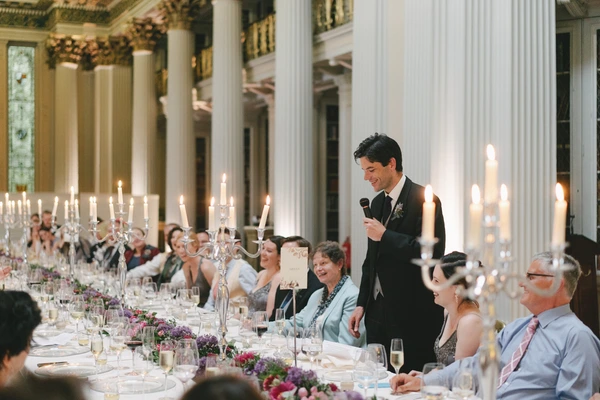 Groom gives a speech at the ornate wedding banquet — white columns, candelabra and floral decoration