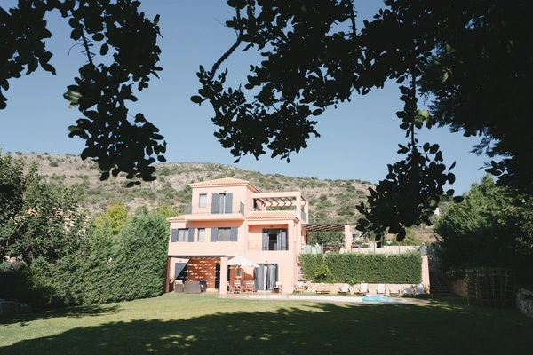 Coral-coloured Mediterranean villa in green gardens with pool and hillside panorama