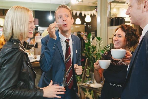 Guests chat and laugh at the wedding reception, holding cups amid decorations and green plants