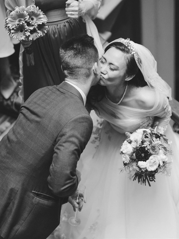 Bride kisses the groom lovingly at the wedding — floral crown, ruffled gown, bouquet in hand