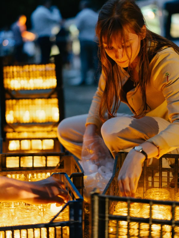 Woman holding candle lantern at evening wedding with warm golden lighting and guests.