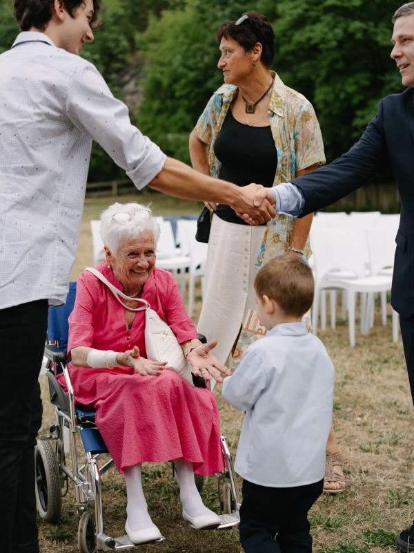 Elderly lady in a pink dress is smiling at a young boy. Wedding reception candid photo.