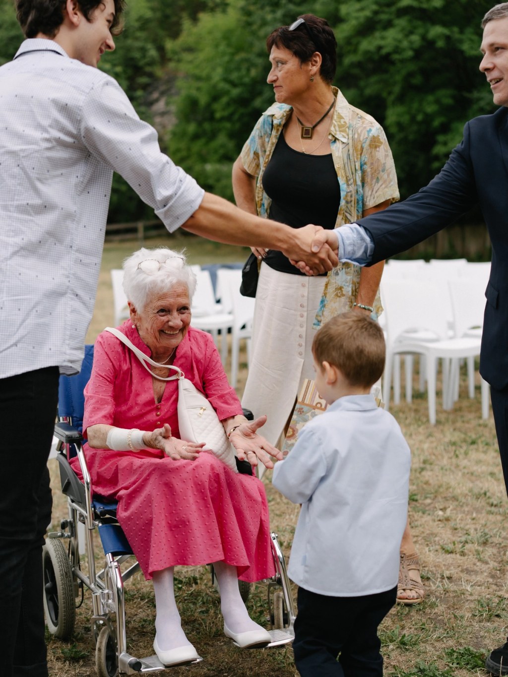Elderly lady in a pink dress is smiling at a young boy. Wedding reception candid photo.