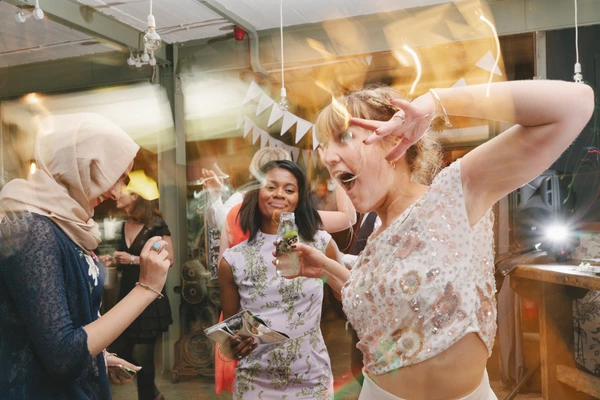 Woman in a checked beaded top laughing and dancing — others smiling with glasses in hand
