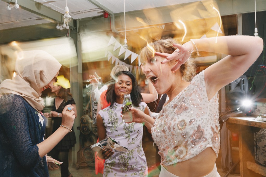 Woman in a checked beaded top laughing and dancing — others smiling with glasses in hand
