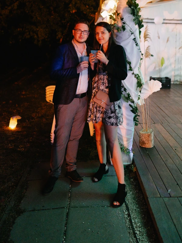 Couple holding drinks at wedding party — evening outdoor celebration, warm atmospheric lighting, festive moment.