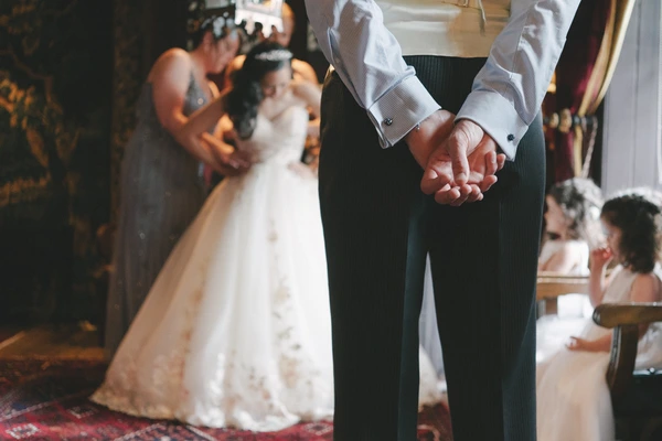 Groom's hands lovingly holding the couple's hands at the altar — white lace gown in background