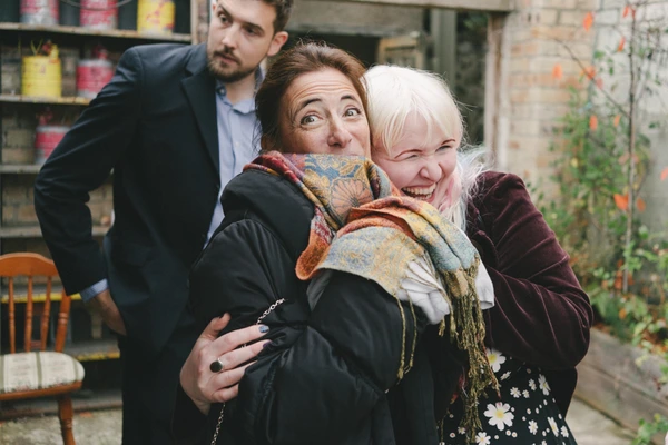 Joyful family moment in a garden — middle-aged woman, white-haired older lady, man hugging them
