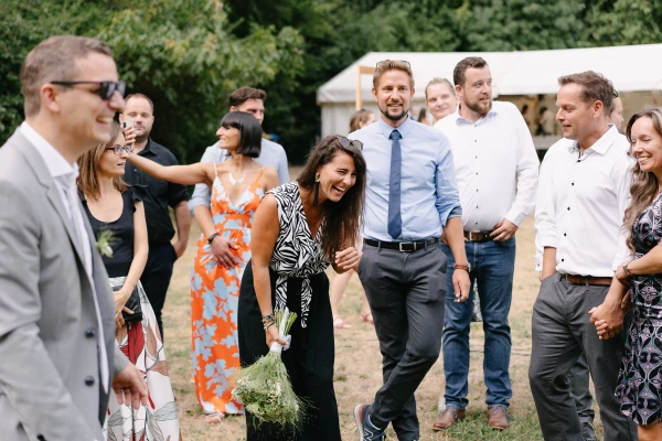 Wedding guests laughing together at outdoor reception with bride and groom in garden venue setting.