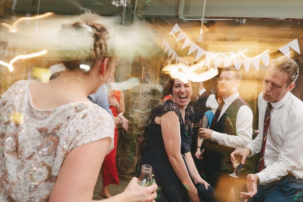 Joyful guests in a decorated hallway — woman in white sequins laughing, men in suits beside her