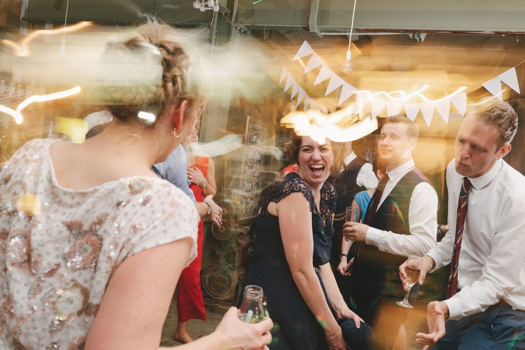Joyful guests in a decorated hallway — woman in white sequins laughing, men in suits beside her