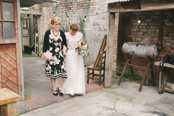 Bride and her mother walk lovingly through an industrial courtyard — old brick walls, warm light
