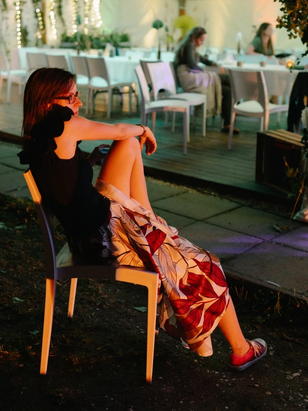 Wedding guest relaxing at outdoor venue — evening ambient lighting, colorful chair, garden reception setting.