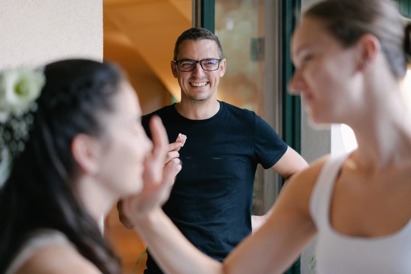 Candid moment of a smiling man in glasses watching the bride's morning preparations. Documentary wedding photography.