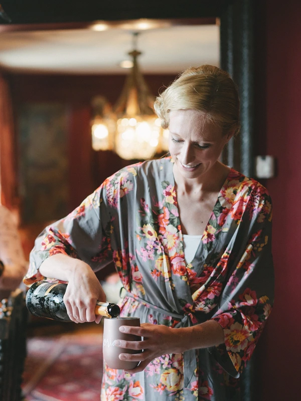Woman in floral kimono pours champagne — warm room light, celebratory moment