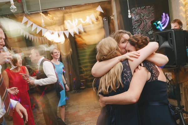Celebrating guests embrace at the reception — white flags and warm light on the dance floor