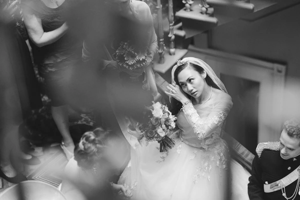 Bride in lace and veil with bouquet, pensive look — family and guests around her in tight space