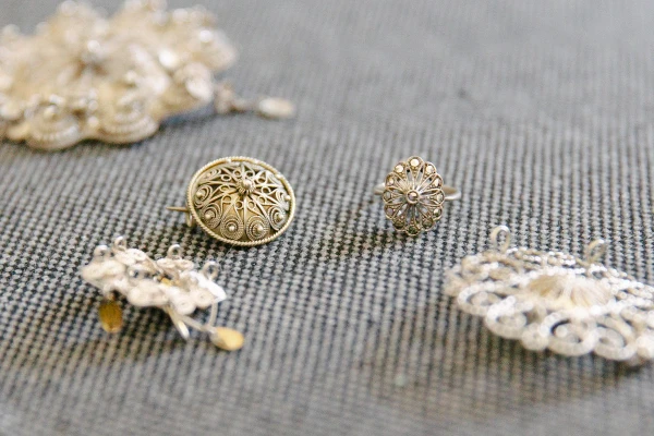 Close-up of the bride's hands pinning a traditional Norwegian silver filigree brooch onto her red bunad vest, lace cuff and silver leaf clasps visible. Wedding detail.