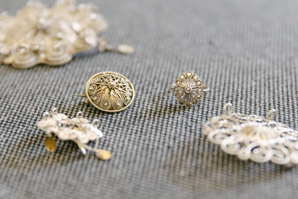 Close-up of the bride's hands pinning a traditional Norwegian silver filigree brooch onto her red bunad vest, lace cuff and silver leaf clasps visible. Wedding detail.