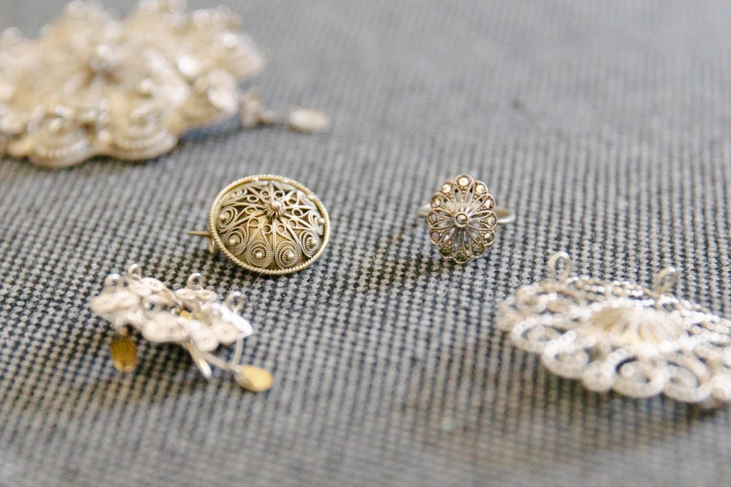Close-up of the bride's hands pinning a traditional Norwegian silver filigree brooch onto her red bunad vest, lace cuff and silver leaf clasps visible. Wedding detail.