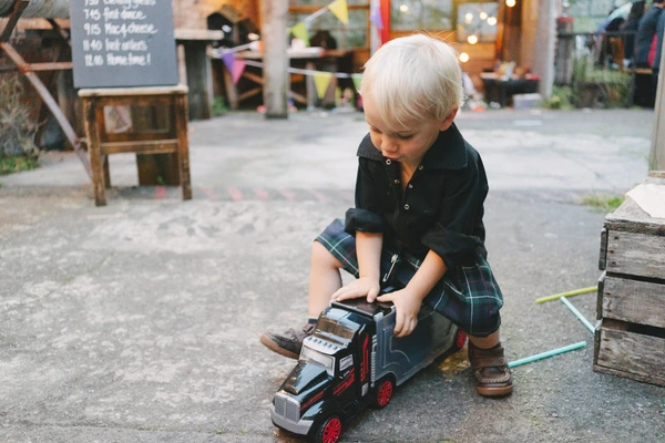 Little girl plays with a toy truck on pebbles at the wedding event — focused, joyful moment