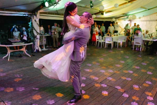 Groom lifting bride during first dance at wedding tent reception with purple uplighting.