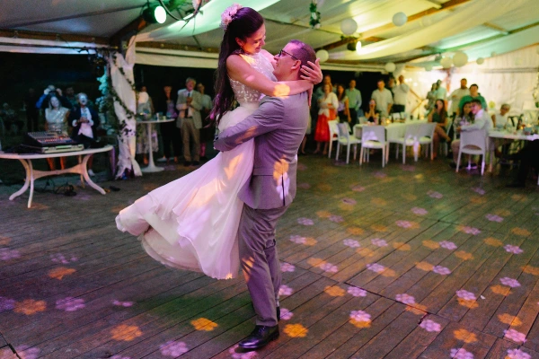 Groom lifting bride during first dance at wedding tent reception with purple uplighting.