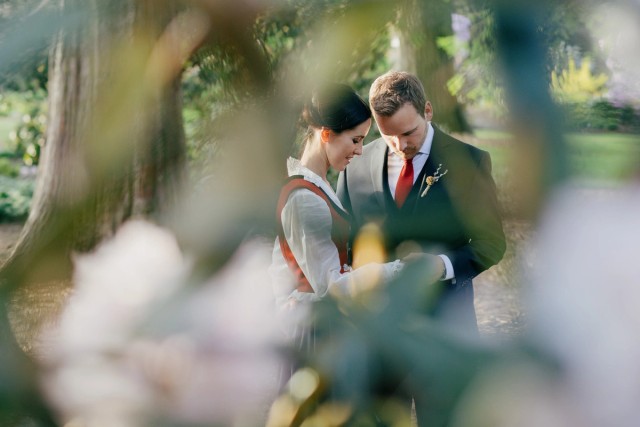 Bride and groom lean foreheads together in the sunlit Royal Botanic Garden, framed by soft blossoms.