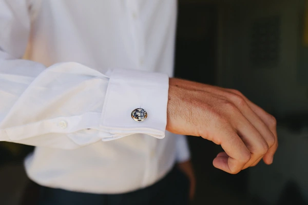Groom's white shirt cuff detail — gold cufflink visible at the wrist, elegant wedding attire